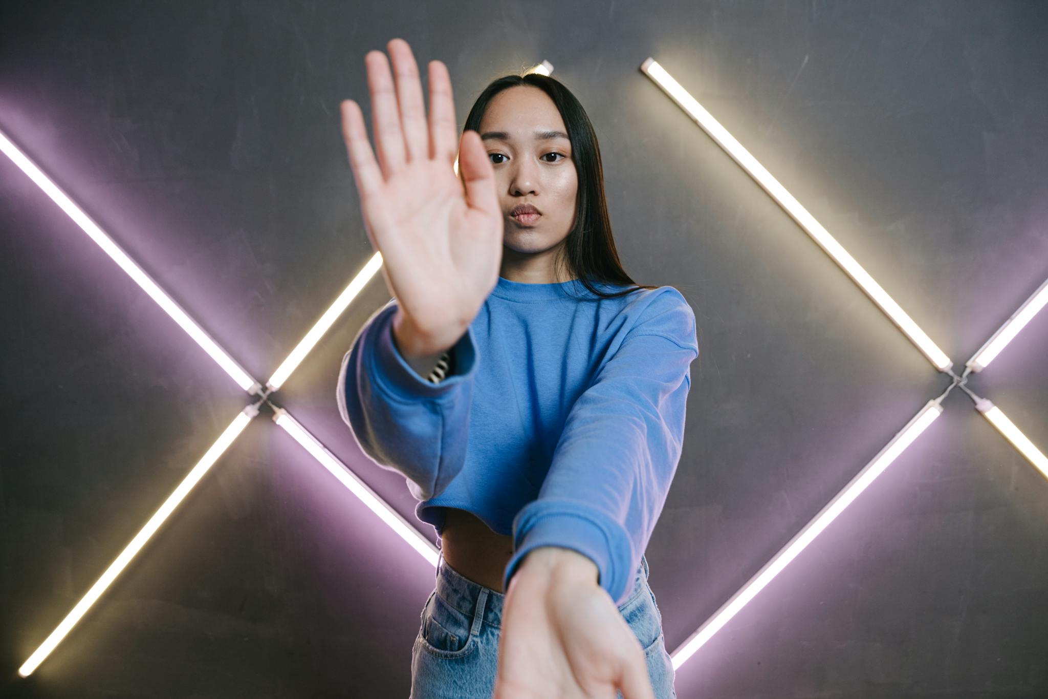 An expressive young Asian woman poses indoors with vibrant purple and white neon lights.